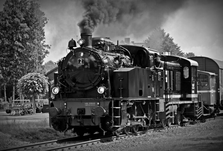 Black and white photo of a classic steam locomotive emitting smoke, evokes nostalgia for historical train travel.